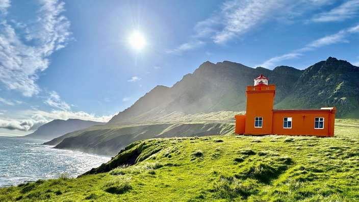 Ein orangefarbener Leuchtturm steht auf einem Hügel mit Blick auf das Meer