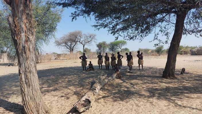 Eine Gruppe von Menschen steht unter einem Baum im Sand