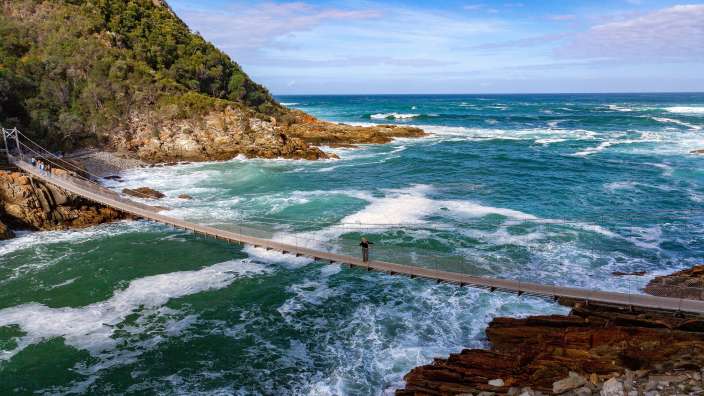 Ein Mann steht auf einer Hängebrücke über das Meer