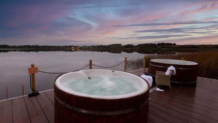 Zwei Whirlpools auf einem Holzdeck neben einem See