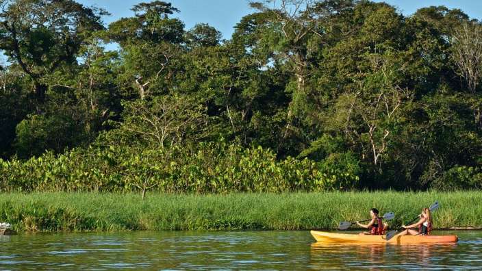 Zwei Menschen paddeln auf einem Fluss mit Bäumen im Hintergrund