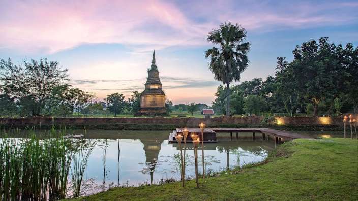 Ein Teich mit Palmen und einem Tempel im Hintergrund
