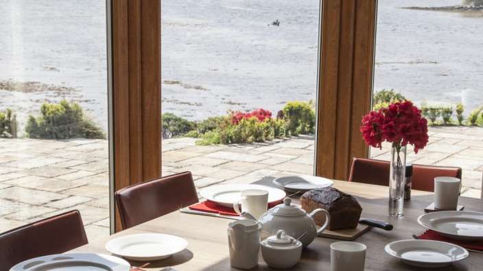 Ein Tisch mit Tellern und Tassen steht vor einem Fenster mit Blick auf den Ozean