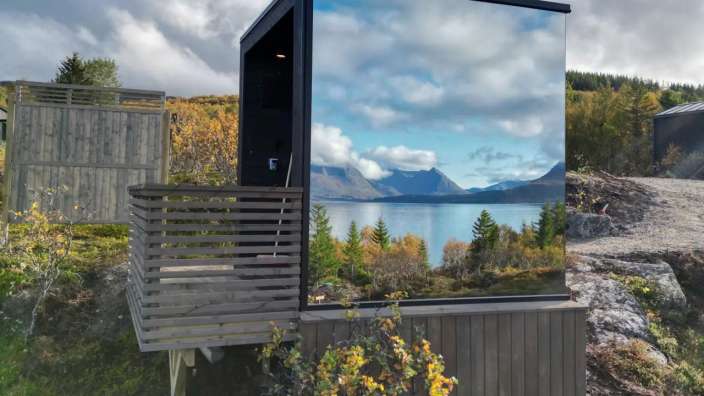 Ein kleines Gebäude mit einem Balkon und einem See dahinter