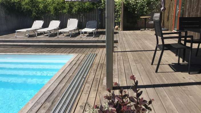Liegestühle stehen auf einem Holzdeck neben einem Swimmingpool