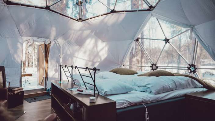 Ein Bett in einem weißen Zelt mit Blick auf den Wald