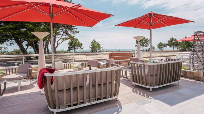 Eine Terrasse mit Möbeln und Regenschirmen mit Blick auf den Strand