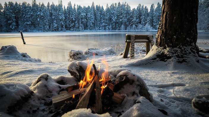 Ein Feuer brennt im Schnee neben einem zugefrorenen See