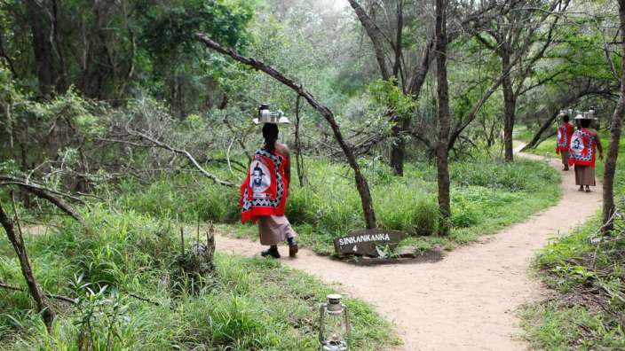 Eine Gruppe von Frauen geht auf einem Pfad in einem Wald mit einem Schild, das swanawana sagt