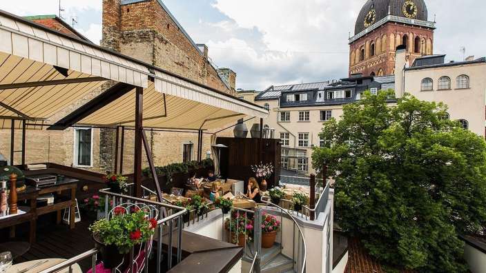 Eine Gruppe von Menschen sitzt auf einem Balkon mit einem Uhrturm im Hintergrund