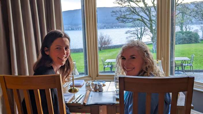 Zwei Frauen sitzen an einem Tisch mit Blick auf einen See