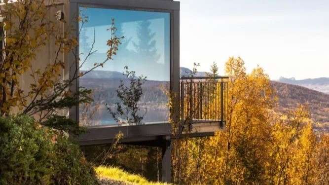 Ein Haus mit einem Balkon und einem großen Fenster in der Mitte eines Waldes .