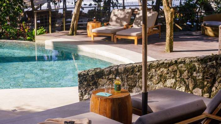 Liegestühle neben einem Swimmingpool mit einer Flasche auf einem Tisch