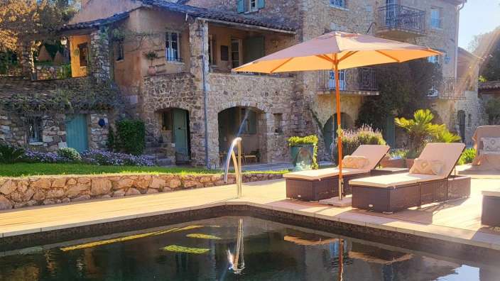Ein Pool mit Liegestühlen und einem Sonnenschirm vor einem Steinhaus