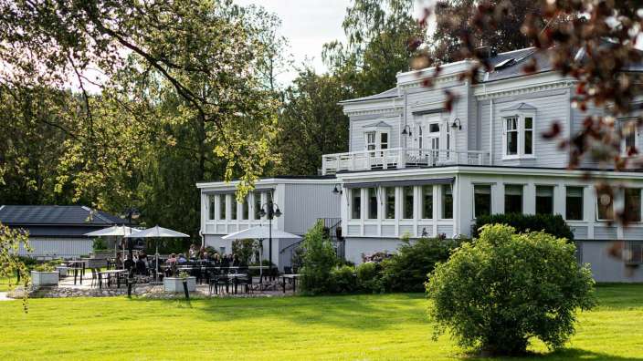 Eine Gruppe von Menschen sitzt auf einer Terrasse vor einem großen weißen Gebäude