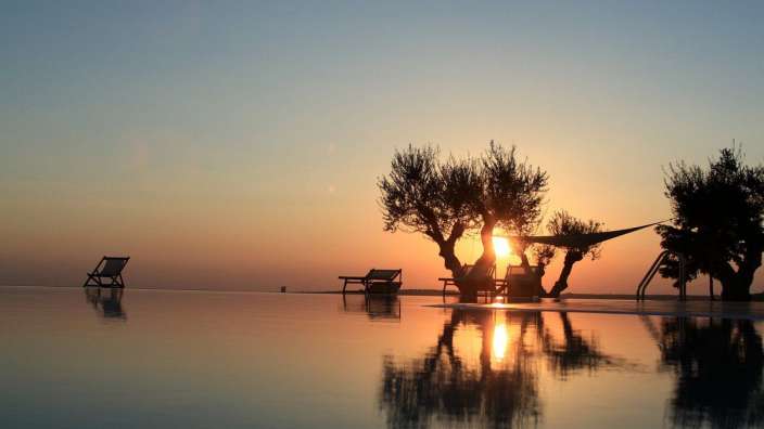 Sonnenuntergang über einem Infinity-Pool mit Liegestühlen und Bäumen