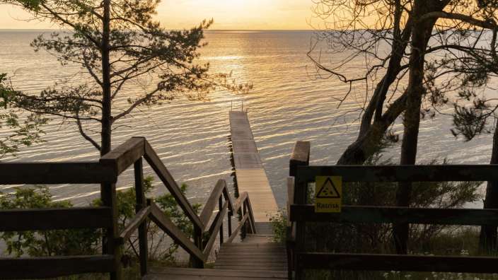 Eine Holztreppe führt hinunter zu einem Pier mit einem Schild darauf , das warnt vor rutschgefahr