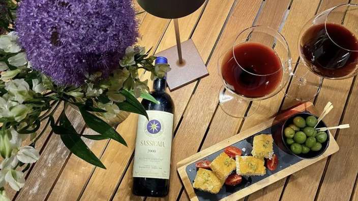 Eine Flasche sassicaia liegt auf einem Holztisch neben zwei Gläsern Wein