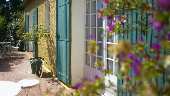 Eine Terrasse mit Tisch und Stühlen vor einem Haus mit blauen Fensterläden