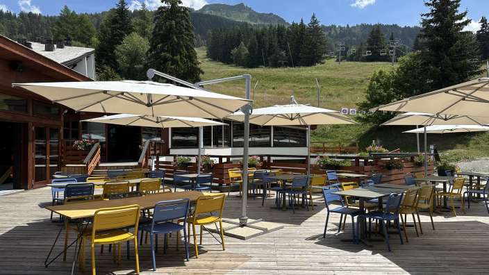 Eine Terrasse mit Tischen und Stühlen und Sonnenschirmen mit einem Berg im Hintergrund