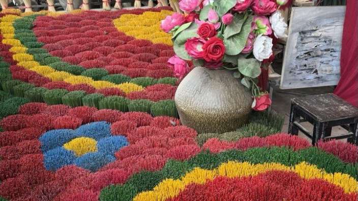 Eine Vase mit Blumen sitzt auf einem Teppich aus bunten Incensesticks