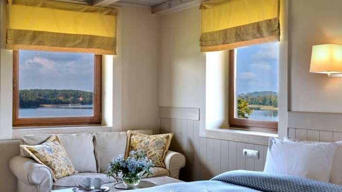 Ein Zimmer mit einem Bett, einem Couchtisch und zwei Fenstern mit Blick auf einen See