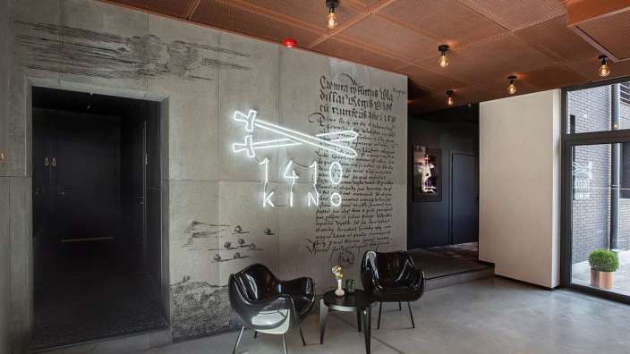 Ein Wohnzimmer mit schwarzen Stühlen und einem Leuchtreklame für das 140 kino