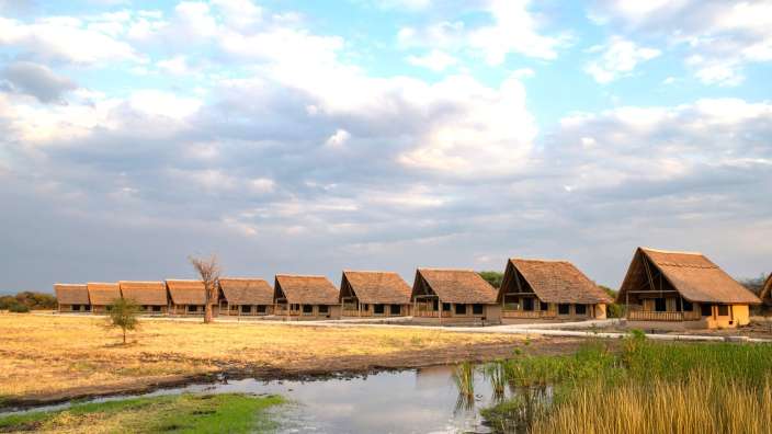 Eine Reihe strohgedeckter Häuser steht neben einem Teich