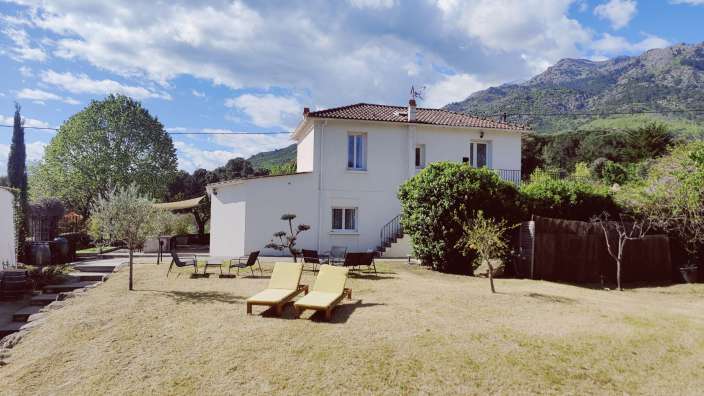 Ein weißes Haus mit einem roten Dach und einem Tisch und Stühlen im Garten