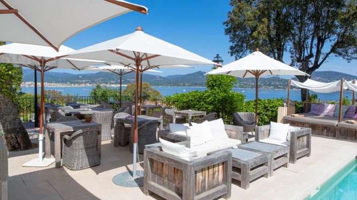 Eine Terrasse mit Möbeln und Sonnenschirmen neben einem Swimmingpool