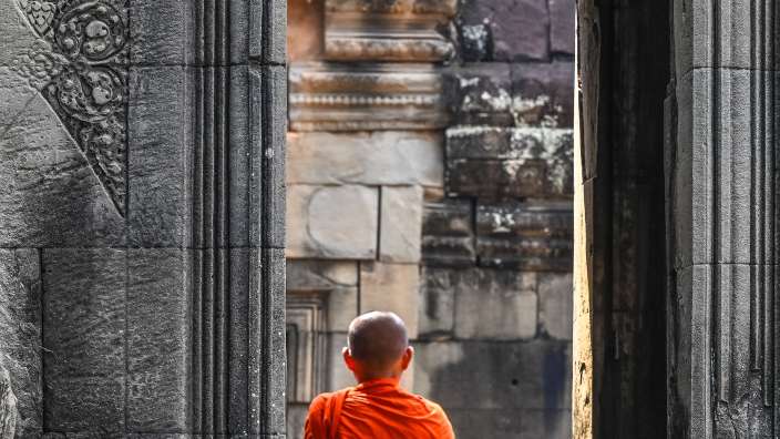 Ein Mann in einem orangefarbenen Kleid schaut aus einem Fenster