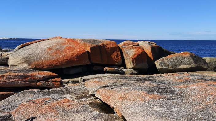Ein großer orangefarbener Felsen sitzt am Ufer des Ozeans