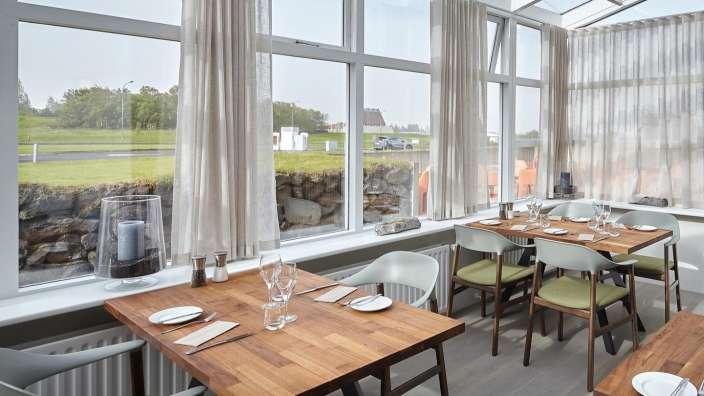 Ein Esszimmer mit Holztischen und Stühlen und vielen Fenstern