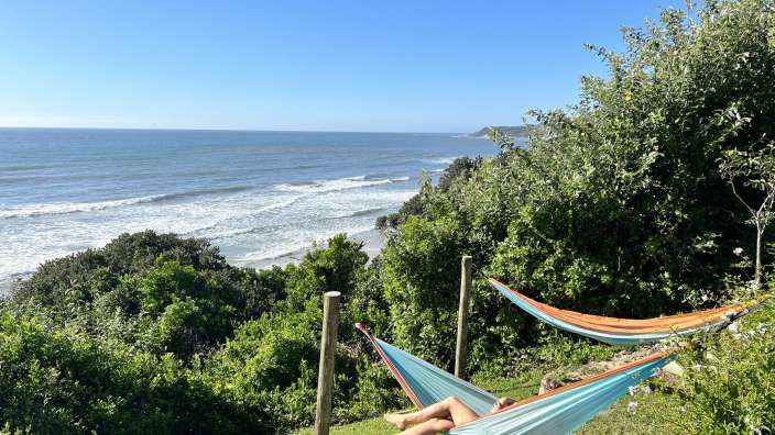 Eine Person liegt in einer Hängematte mit Blick auf das Meer