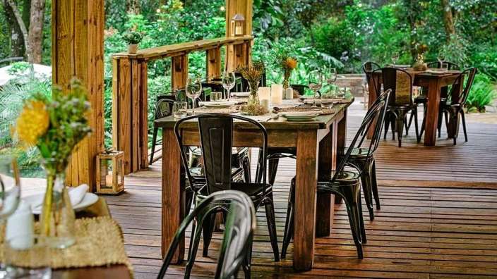 Tische und Stühle auf einem Holzdeck mit Bäumen im Hintergrund