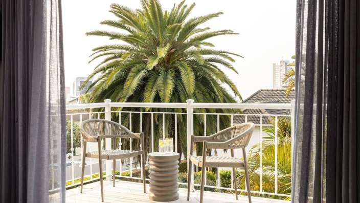 Ein Balkon mit zwei Stühlen und einem Tisch mit einer Palme im Hintergrund