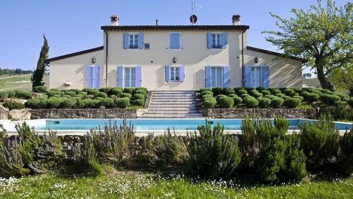 Ein großes weißes Haus mit blauen Fensterläden und einem Pool davor