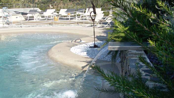 Ein Pool mit einem Wasserfall und Liegestühlen im Hintergrund