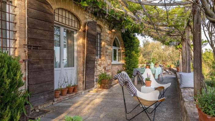 Zwei weiße Schmetterlingsstühle stehen vor einem Steingebäude