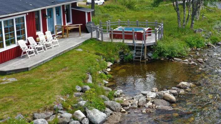 Ein rotes Haus mit einer roten Wanne auf dem Deck neben einem Fluss