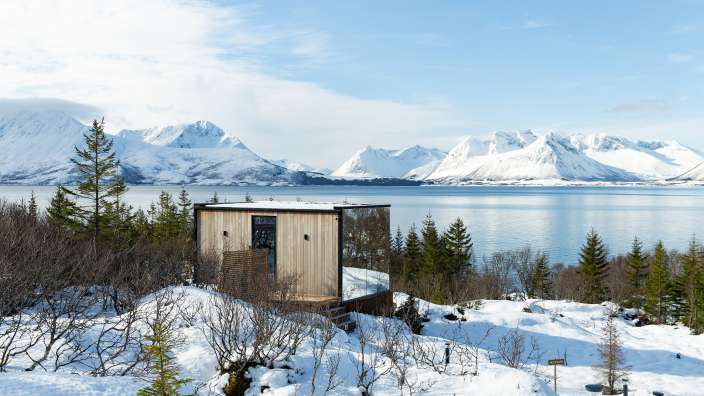 Ein kleines Holzhaus steht inmitten eines schneebedeckten Waldes neben einem See