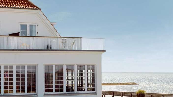 Ein weißes Haus mit vielen Fenstern und einem Balkon mit Blick auf das Meer