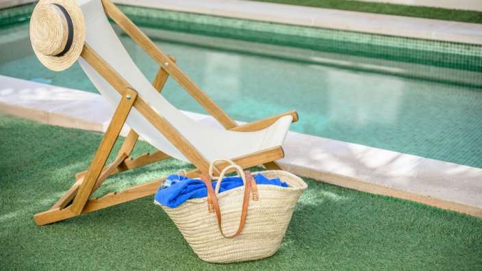 Liegestuhl mit Strohhut und Korb neben einem Pool