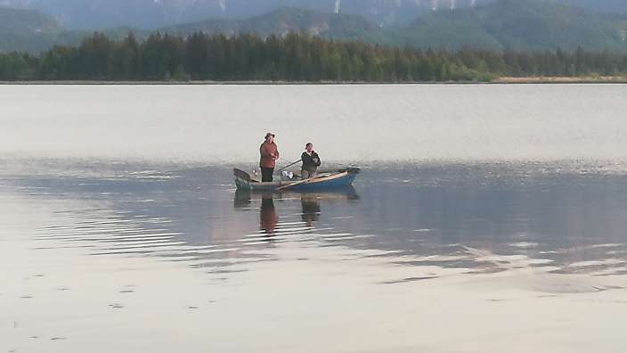 Zwei Männer in einem Boot auf einem See mit Bergen im Hintergrund
