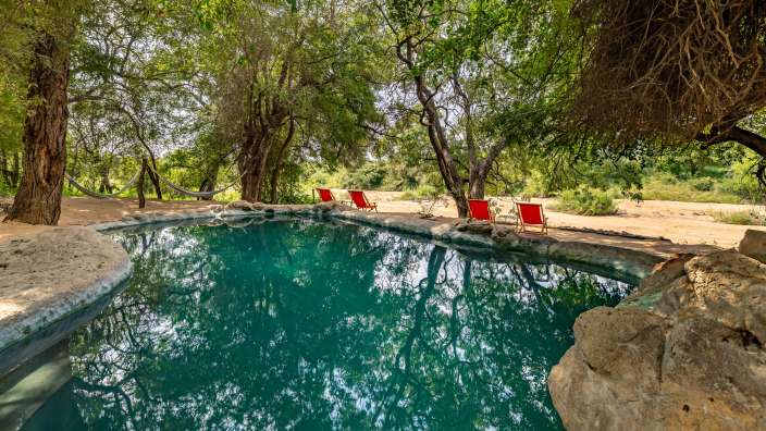 Ein Swimmingpool mit roten Stühlen und einer Hängematte