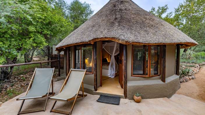 Ein Strohdachhaus mit zwei Liegestühlen davor