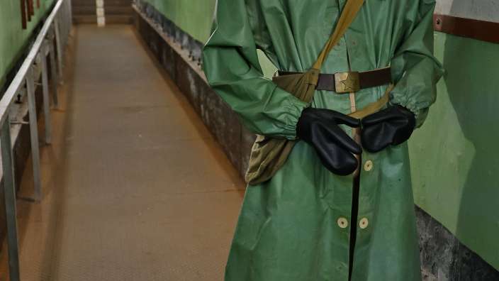 Ein Mann in einer Gasmaske und einem grünen Mantel steht in einem Tunnel