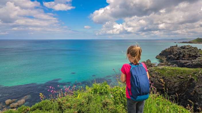 Ein kleines Mädchen mit einem blauen Rucksack schaut auf das Meer