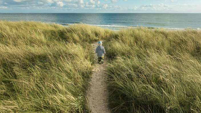 Ein kleiner Junge geht einen Sandweg hinunter zu einem Strand