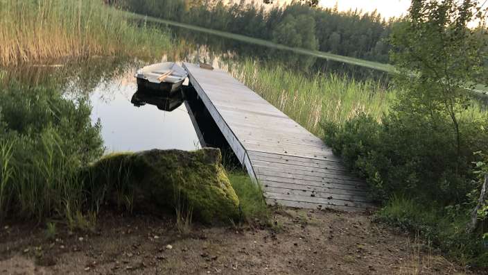 Ein weißes Boot sitzt auf einem Holzsteg in einem See